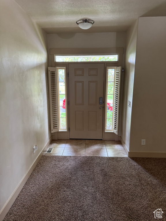 Entryway with light carpet, light tile patterned floors, and a textured ceiling
