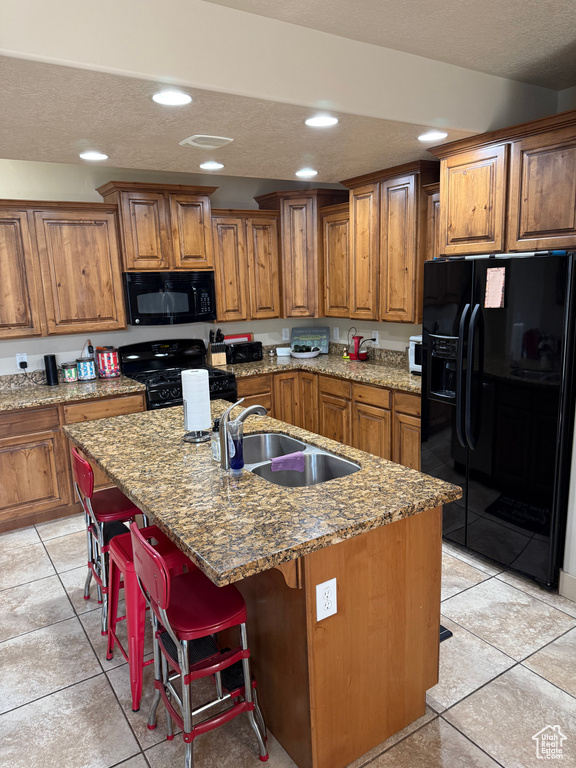 Kitchen with black appliances, brown cabinetry, light tile patterned floors, recessed lighting, and a textured ceiling