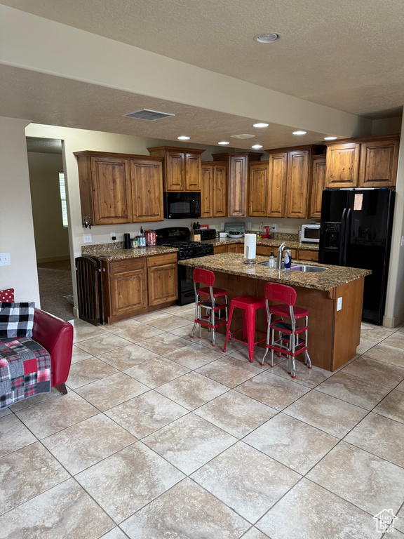 Kitchen featuring black appliances, brown cabinets, a center island with sink, a breakfast bar area, and recessed lighting