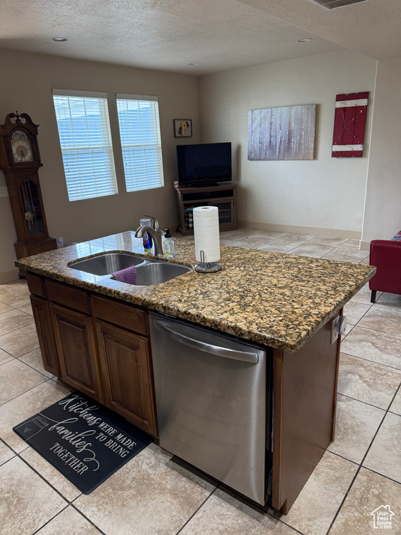 Kitchen featuring dishwasher, a center island with sink, a textured ceiling, light tile patterned flooring, and stone countertops