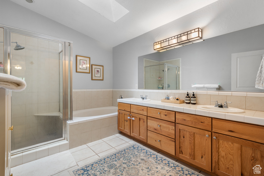 Full bathroom featuring a skylight, lofted ceiling, a stall shower, tile patterned floors, and double vanity