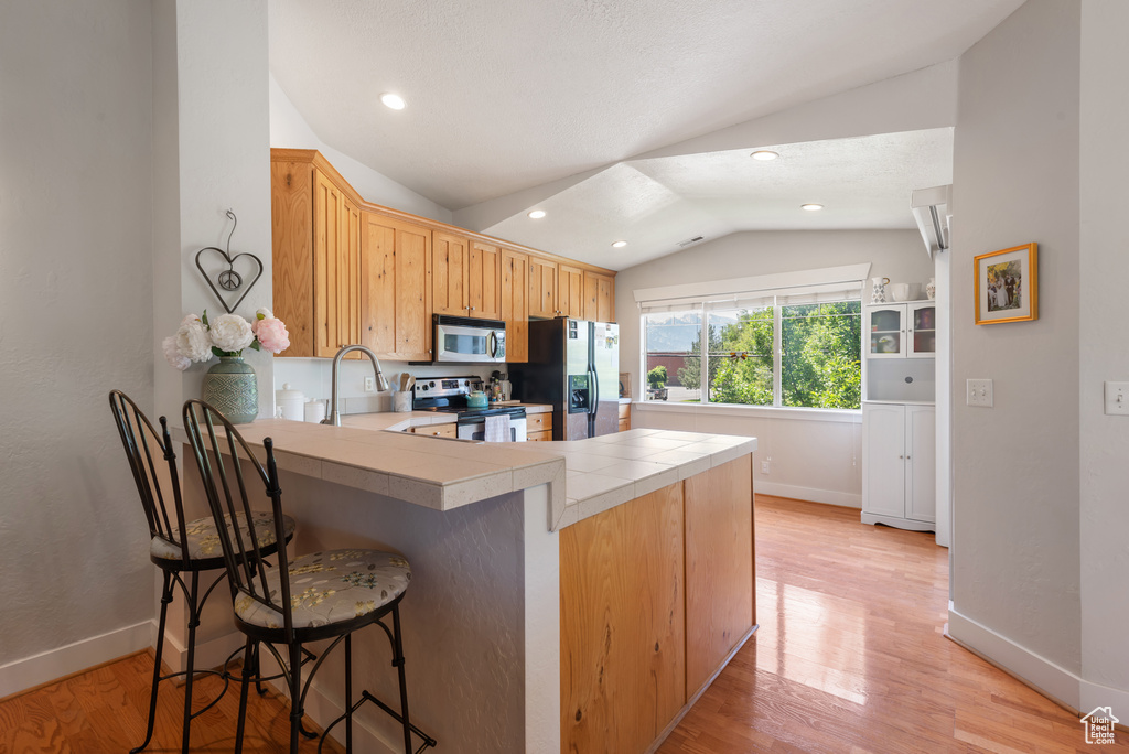 Kitchen with appliances with stainless steel finishes, vaulted ceiling, a peninsula, light wood-style floors, and a kitchen breakfast bar