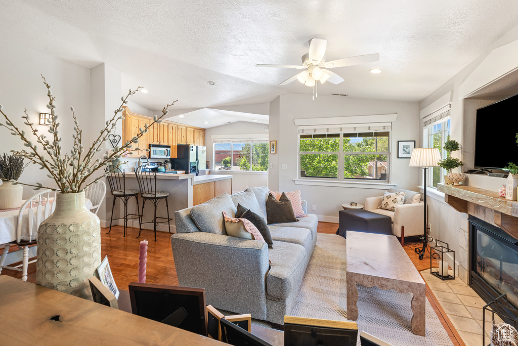 Living area featuring vaulted ceiling, a tile fireplace, a ceiling fan, light wood-style floors, and a textured ceiling