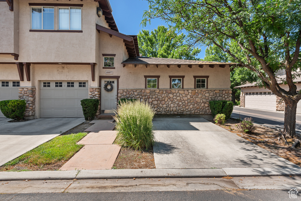 View of front of property with stucco siding, stone siding, a garage, and concrete driveway
