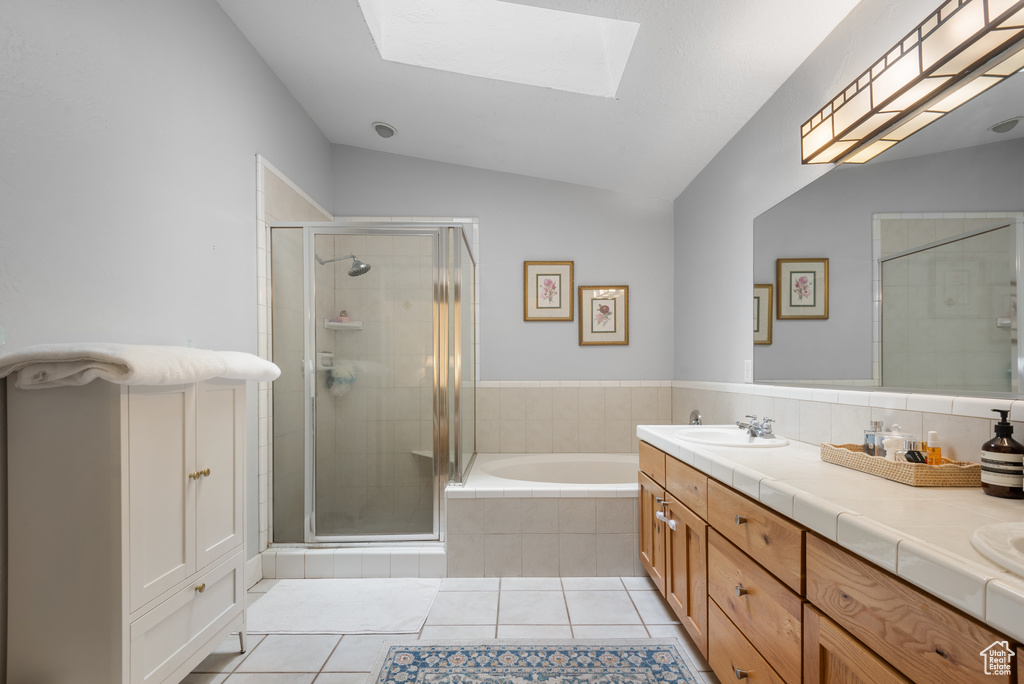 Bathroom with a bath, a stall shower, tile patterned floors, a skylight, and double vanity