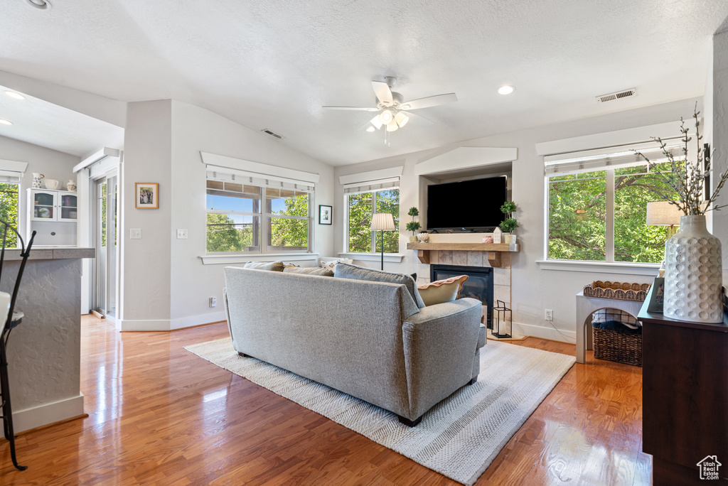 Living room featuring vaulted ceiling, a ceiling fan, healthy amount of natural light, a tiled fireplace, and light wood-style floors