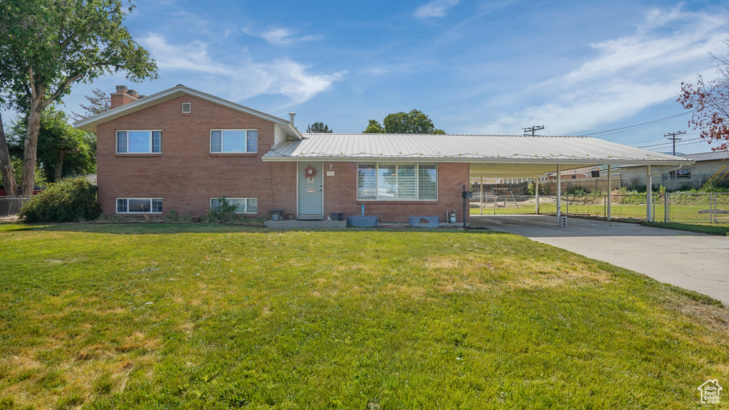 Split level home featuring brick siding, an attached carport, driveway, a metal roof, and a chimney