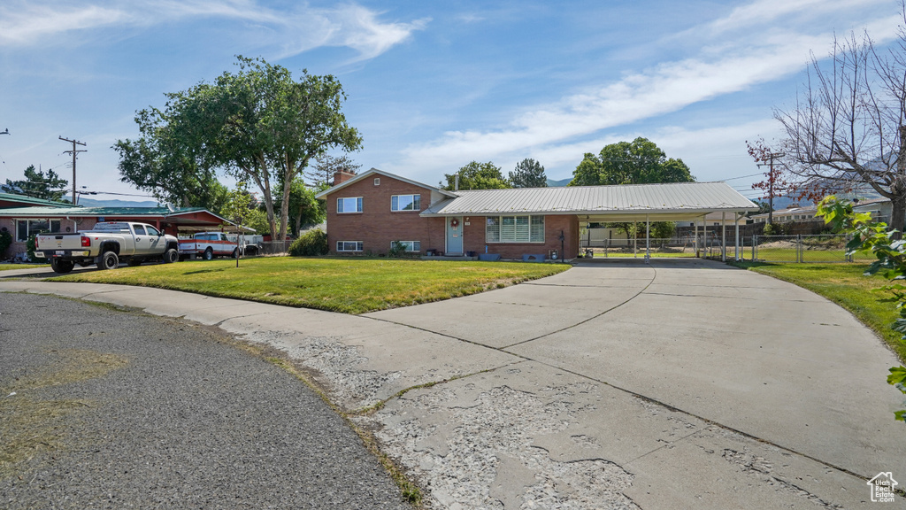 View of front facade featuring driveway, an attached carport, brick siding, and a metal roof