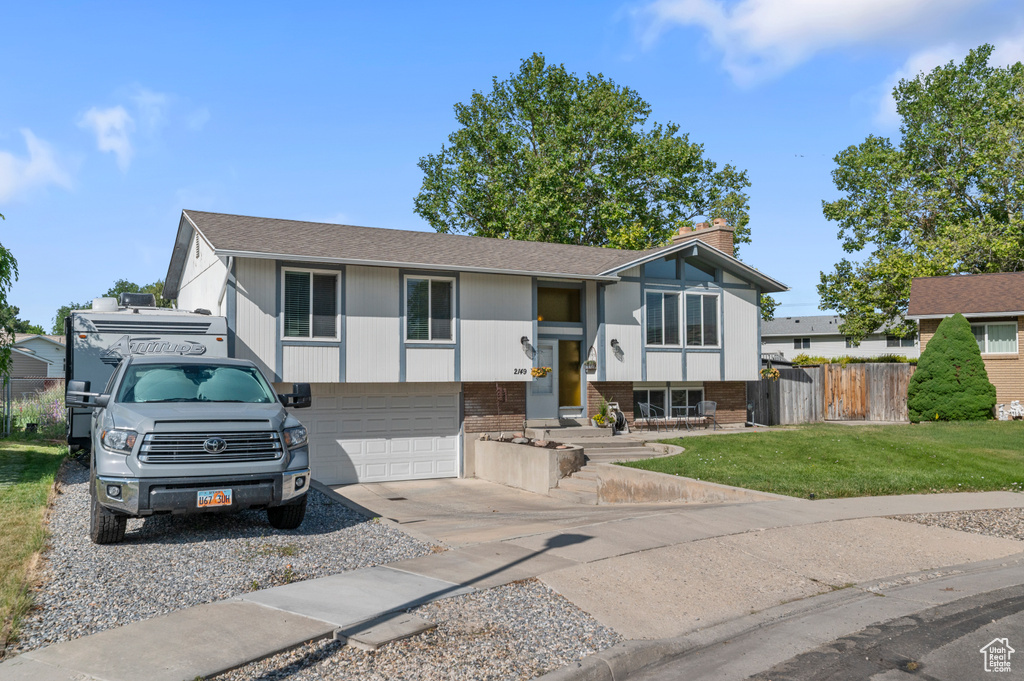 Raised ranch featuring brick siding, driveway, a chimney, a garage, and a shingled roof