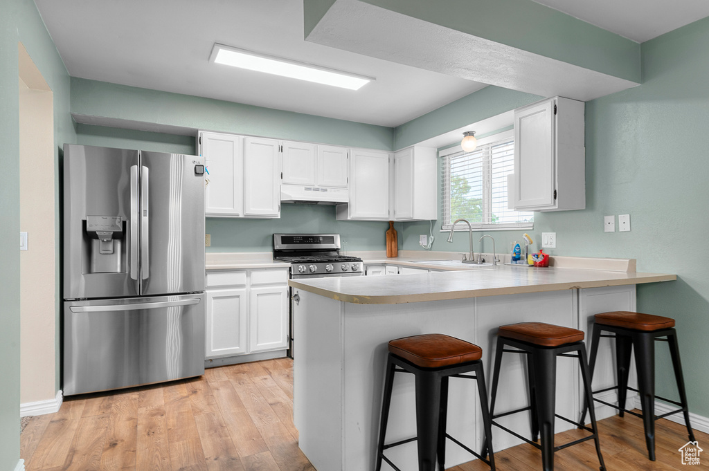 Kitchen featuring stainless steel appliances, under cabinet range hood, a peninsula, and white cabinets
