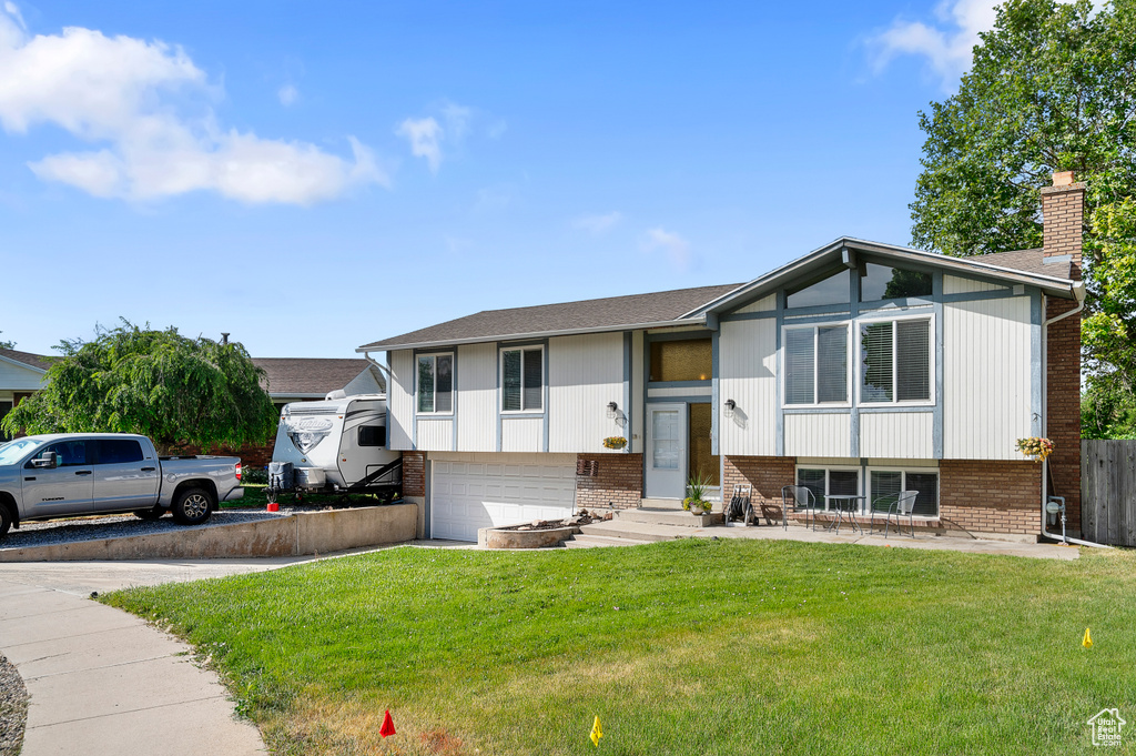 Raised ranch featuring brick siding, driveway, an attached garage, and a chimney