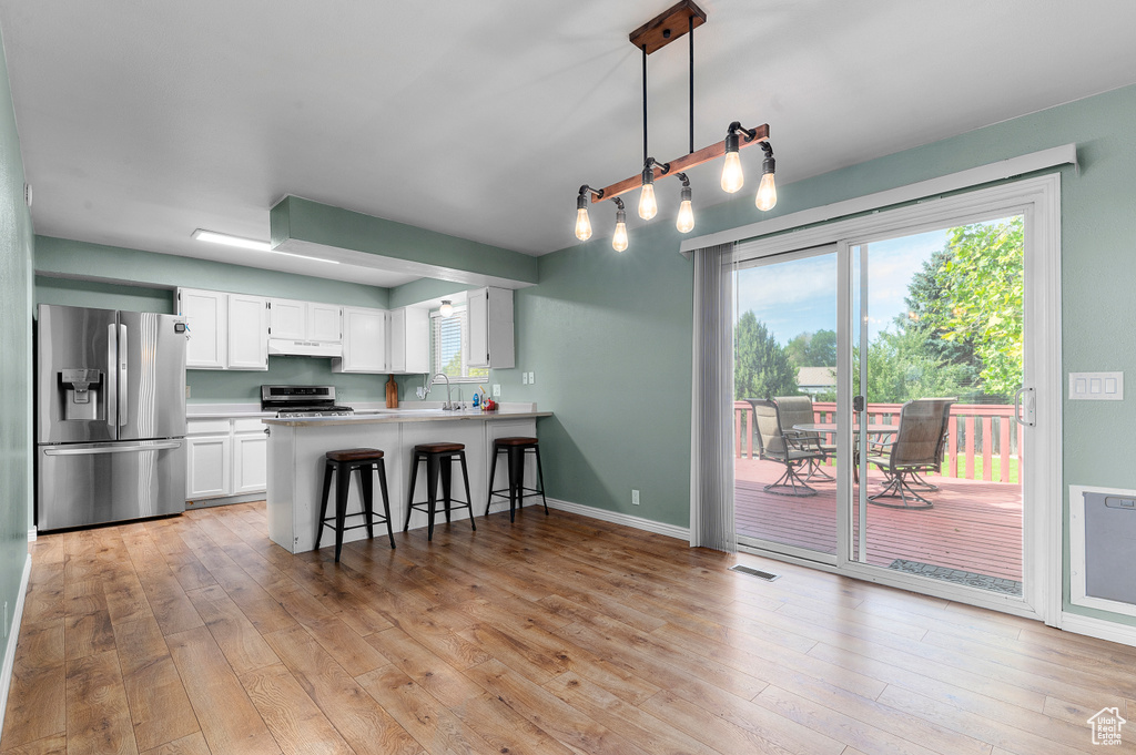 Kitchen with appliances with stainless steel finishes, light wood-type flooring, a peninsula, and under cabinet range hood