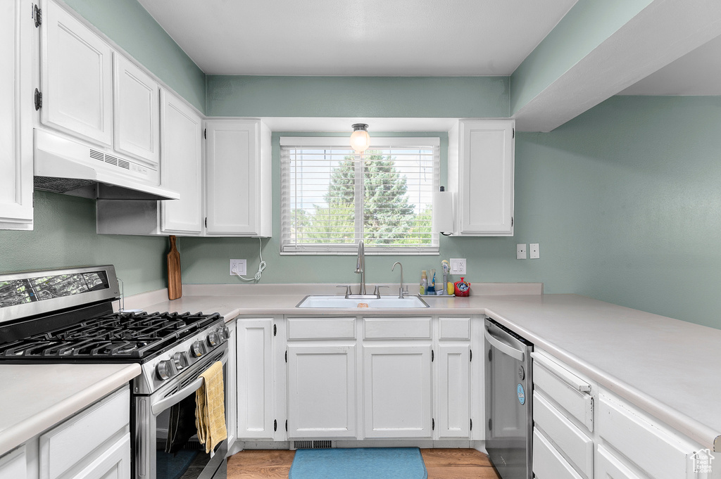 Kitchen featuring appliances with stainless steel finishes, under cabinet range hood, white cabinets, and light countertops