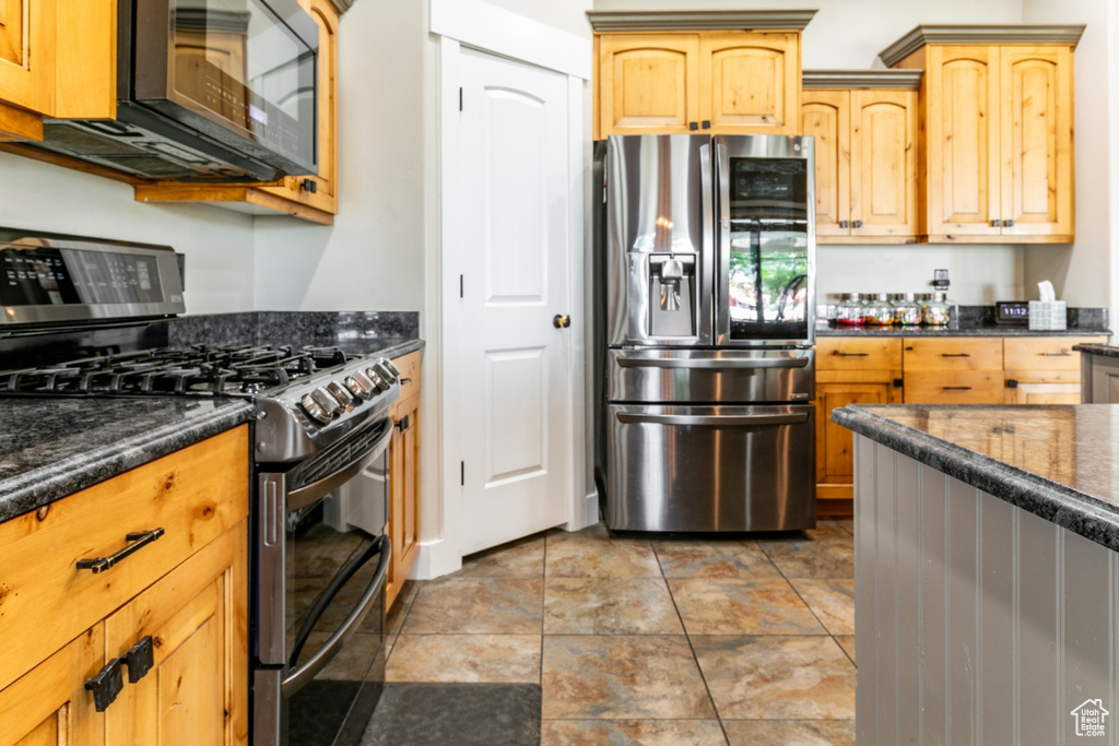 Kitchen with stainless steel appliances, dark stone countertops, and light brown cabinets