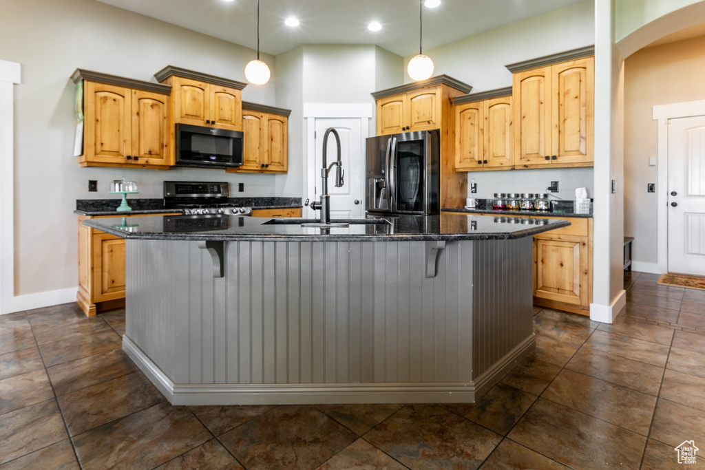 Kitchen featuring black microwave, fridge with ice dispenser, gas stove, arched walkways, and an island with sink