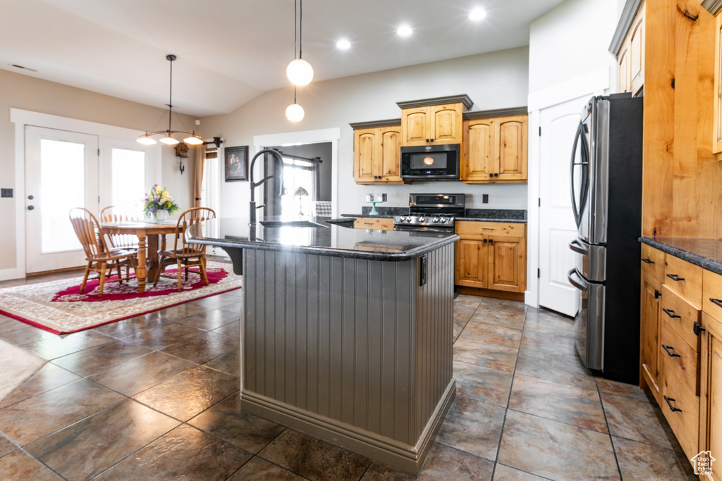 Kitchen featuring stainless steel appliances, a center island with sink, vaulted ceiling, pendant lighting, and dark stone countertops