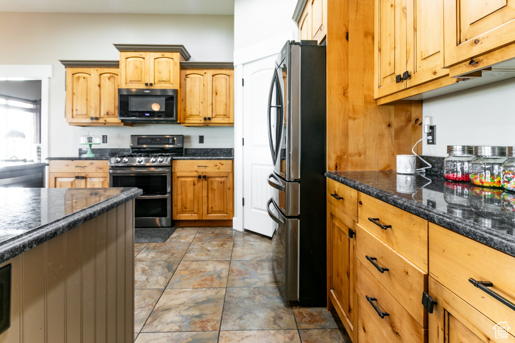 Kitchen with appliances with stainless steel finishes, dark stone countertops, and stone finish flooring