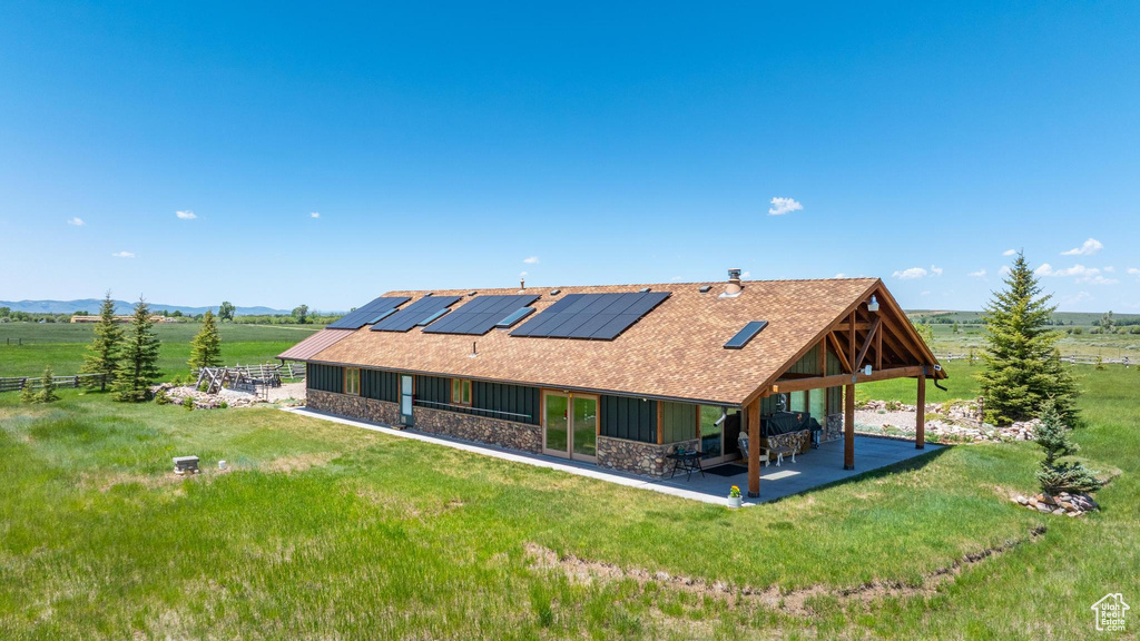 Back of property with stone siding, a patio, solar panels, a lawn, and a view of rural / pastoral area