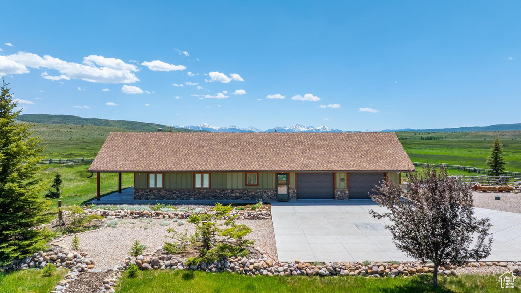 View of front facade with an attached garage, concrete driveway, stone siding, a mountain view, and roof with shingles