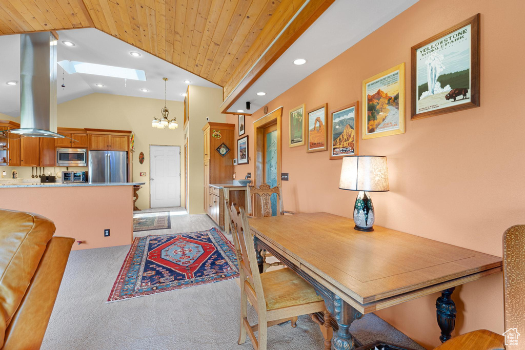 Dining space with a skylight, vaulted ceiling, a chandelier, light colored carpet, and wood ceiling