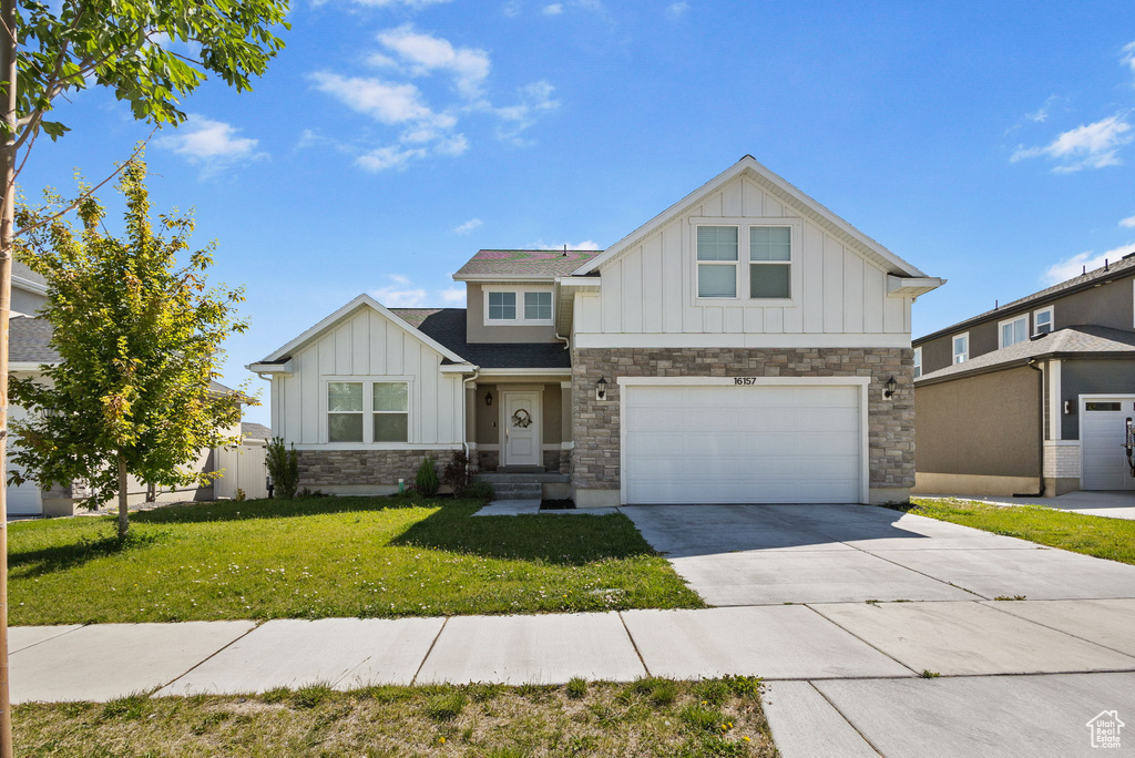 View of front of house with board and batten siding, stone siding, driveway, an attached garage, and a front yard
