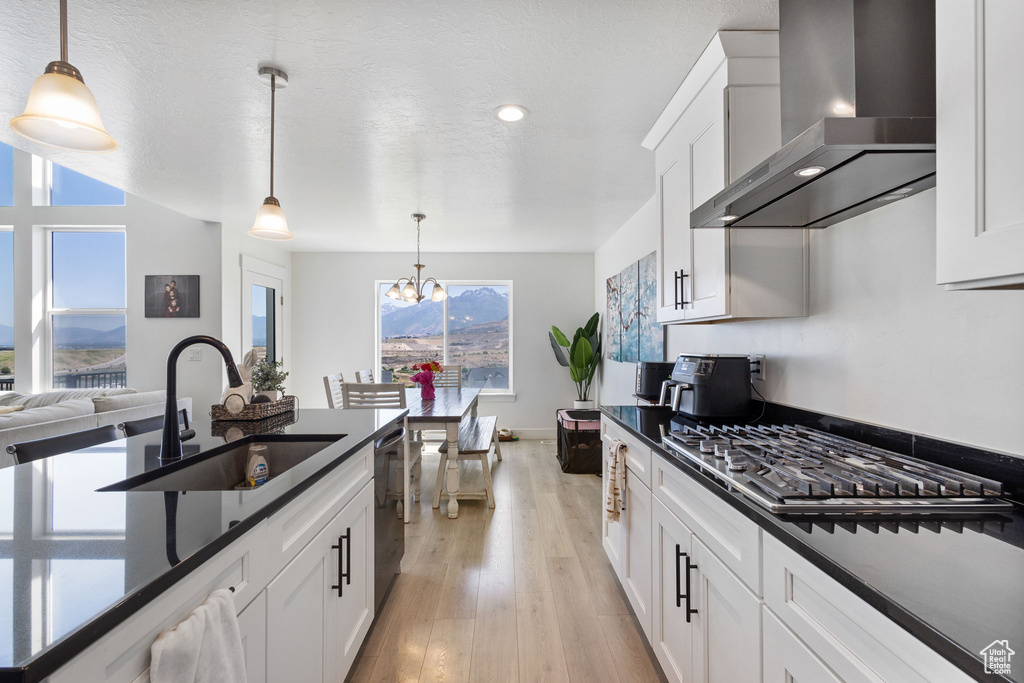 Kitchen with wall chimney range hood, dark countertops, appliances with stainless steel finishes, white cabinets, and a chandelier