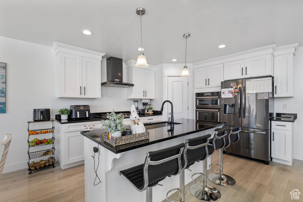 Kitchen with stainless steel fridge, wall chimney range hood, light wood-style flooring, dark countertops, and recessed lighting