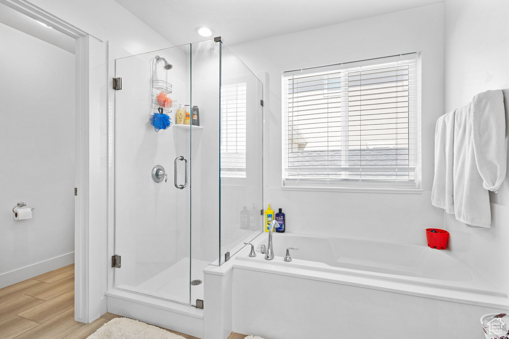 Full bath featuring a stall shower, plenty of natural light, a garden tub, and wood finished floors