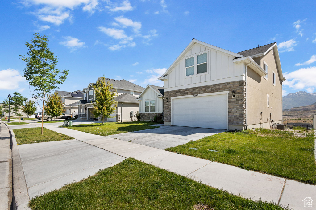 View of front facade featuring board and batten siding, an attached garage, driveway, and a front yard