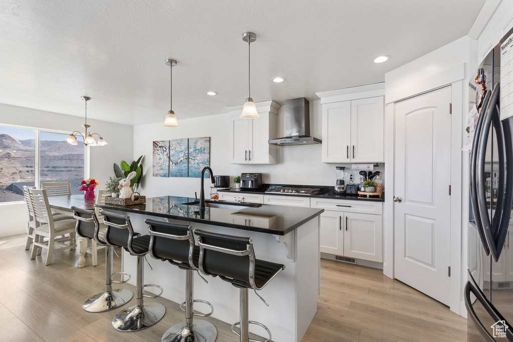 Kitchen with wall chimney exhaust hood, light wood-style floors, a breakfast bar, white cabinets, and recessed lighting