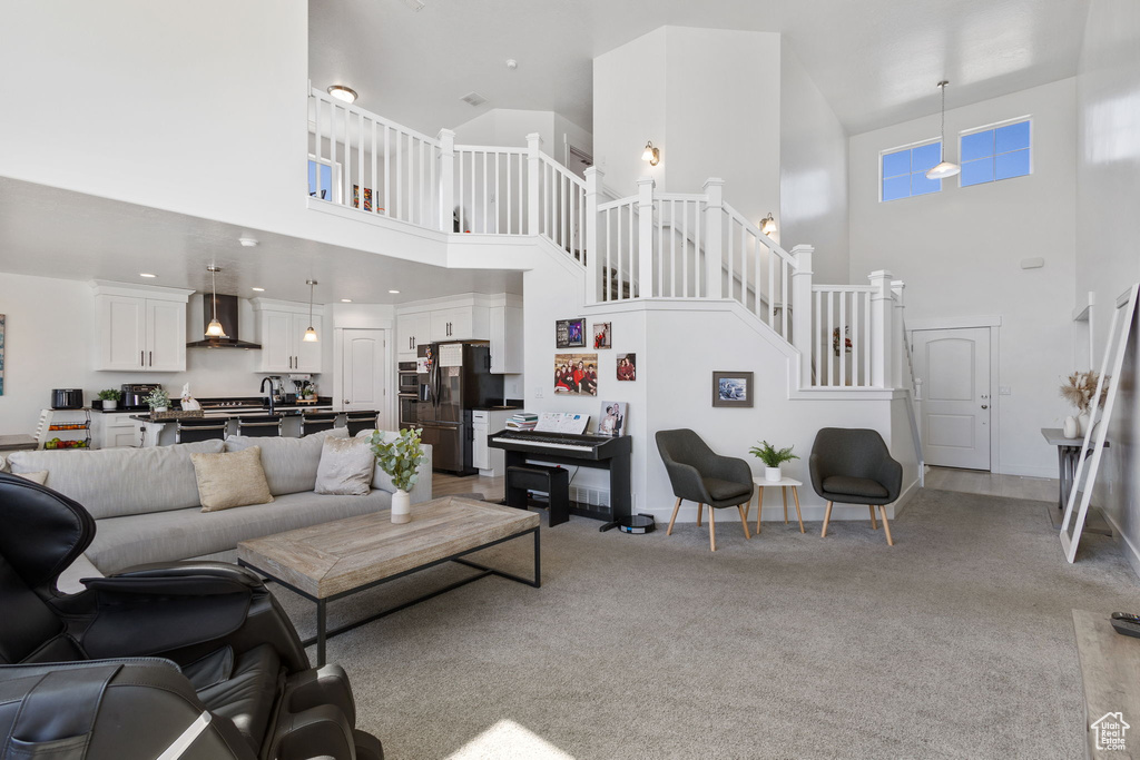 Living room featuring a towering ceiling, stairway, and light colored carpet