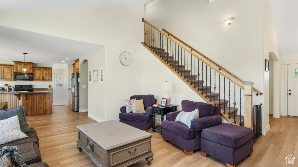 Living area with high vaulted ceiling, stairway, arched walkways, light wood finished floors, and recessed lighting