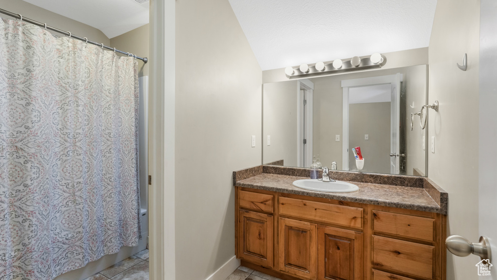 Full bath featuring tile patterned floors, vanity, curtained shower, and lofted ceiling