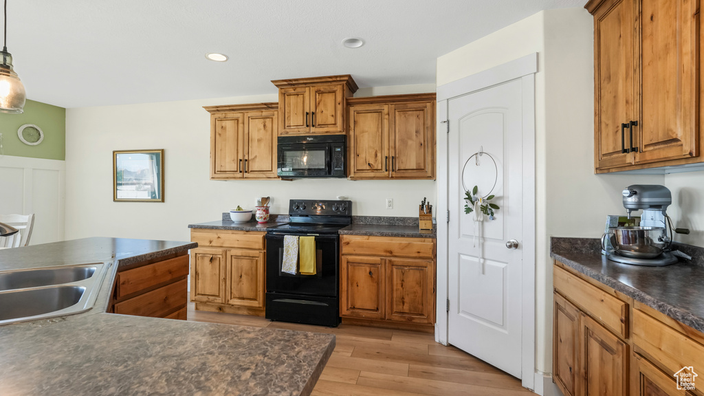 Kitchen featuring black appliances, dark countertops, brown cabinetry, light wood-type flooring, and recessed lighting