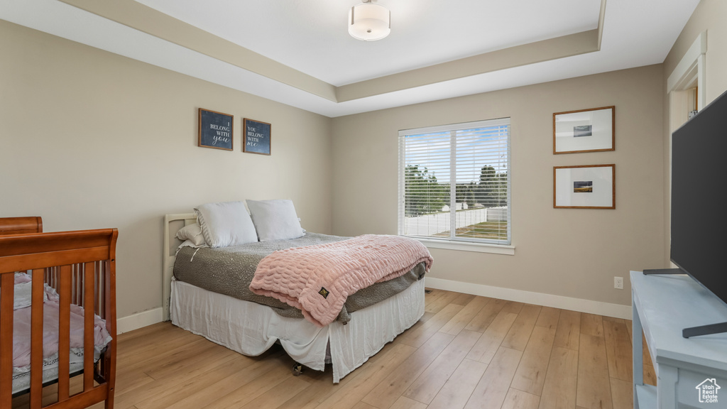 Bedroom with a raised ceiling and light wood-type flooring