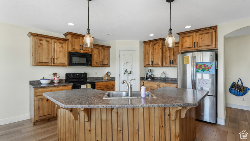 Kitchen with black appliances, light wood-style flooring, dark countertops, a kitchen breakfast bar, and recessed lighting