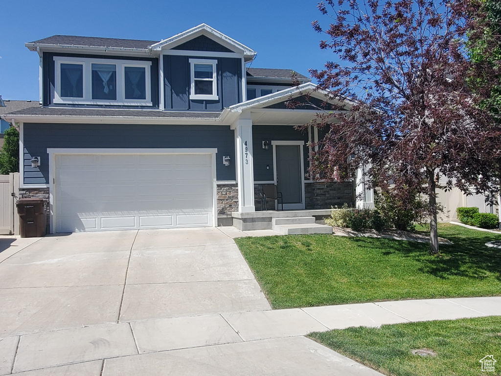 View of front of home with a front yard, driveway, stone siding, and a garage
