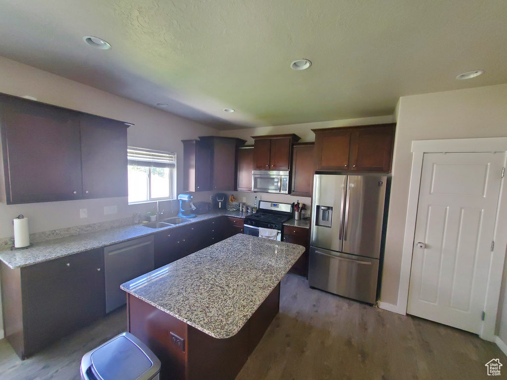 Kitchen featuring stainless steel appliances, a kitchen island, dark wood-style flooring, light stone counters, and recessed lighting
