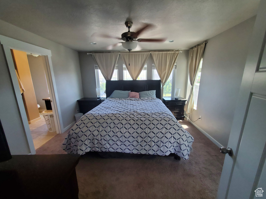 Bedroom with light carpet, multiple windows, a ceiling fan, and connected bathroom