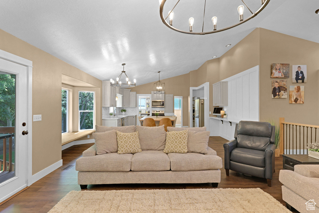 Living room with a chandelier, dark wood-style flooring, and vaulted ceiling