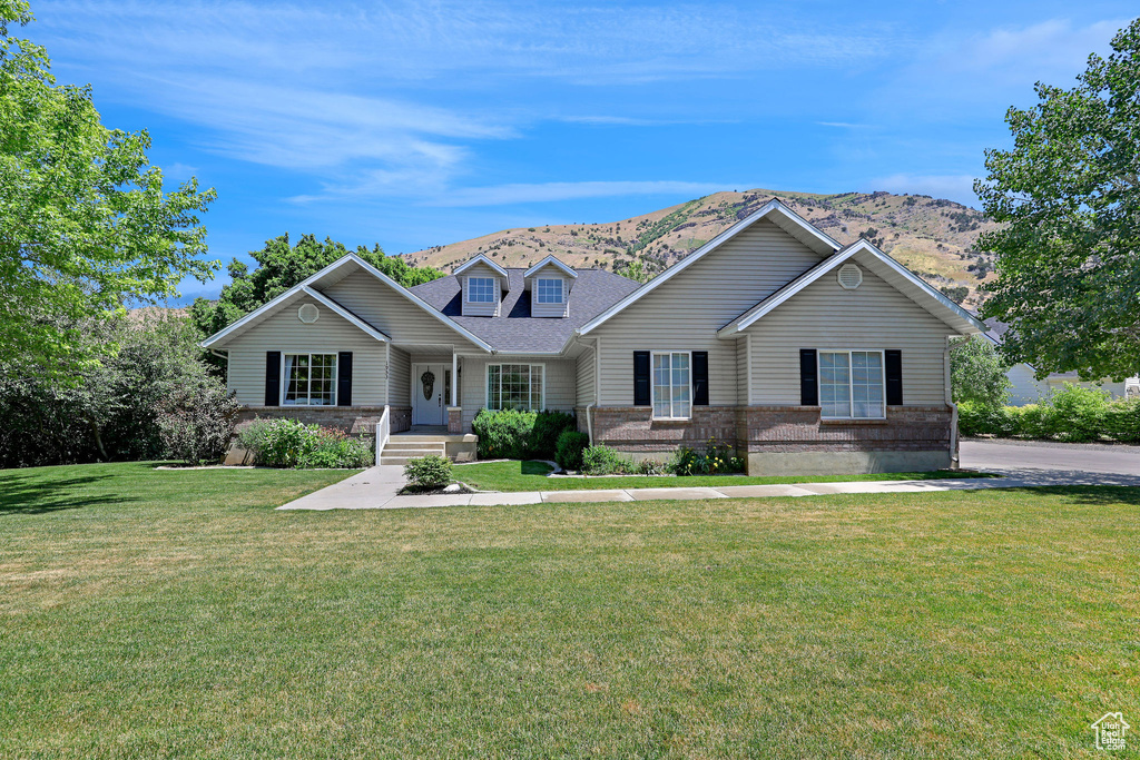 View of front of home featuring a mountain view, a porch, a front yard, a shingled roof, and brick siding