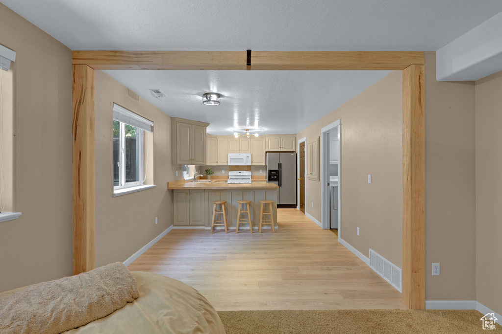 Kitchen featuring stainless steel fridge, white microwave, a peninsula, light countertops, and a breakfast bar area