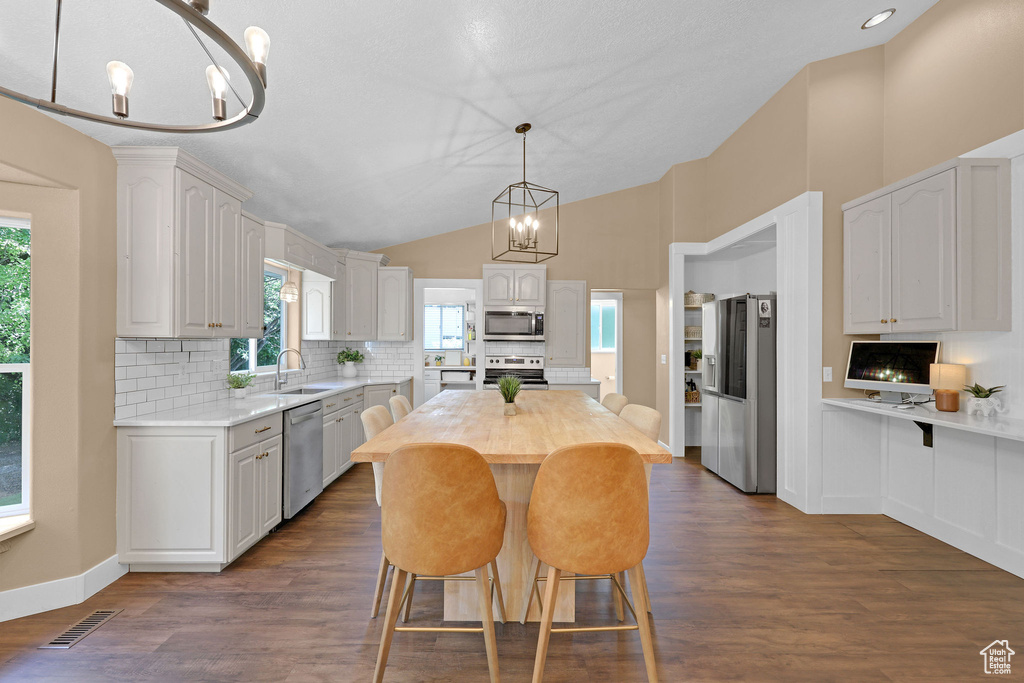 Kitchen with appliances with stainless steel finishes, a chandelier, decorative backsplash, a breakfast bar area, and lofted ceiling