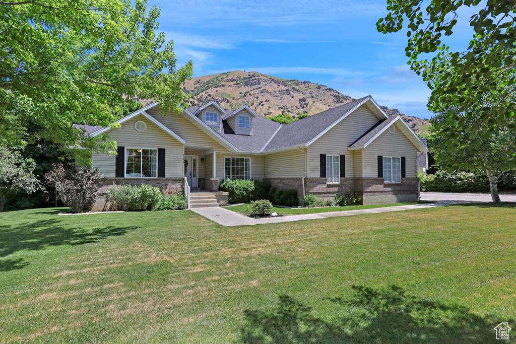 View of front of home with a mountain view, brick siding, a front lawn, and a shingled roof