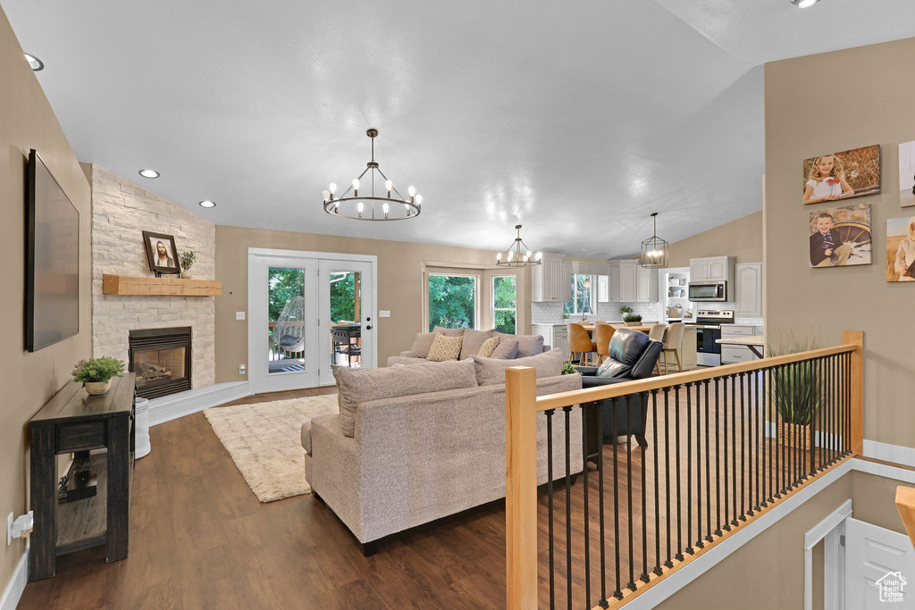 Living room with a chandelier, vaulted ceiling, dark wood-style flooring, a fireplace, and recessed lighting
