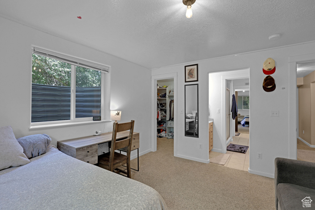Bedroom featuring a walk in closet, a textured ceiling, light colored carpet, a closet, and light tile patterned floors