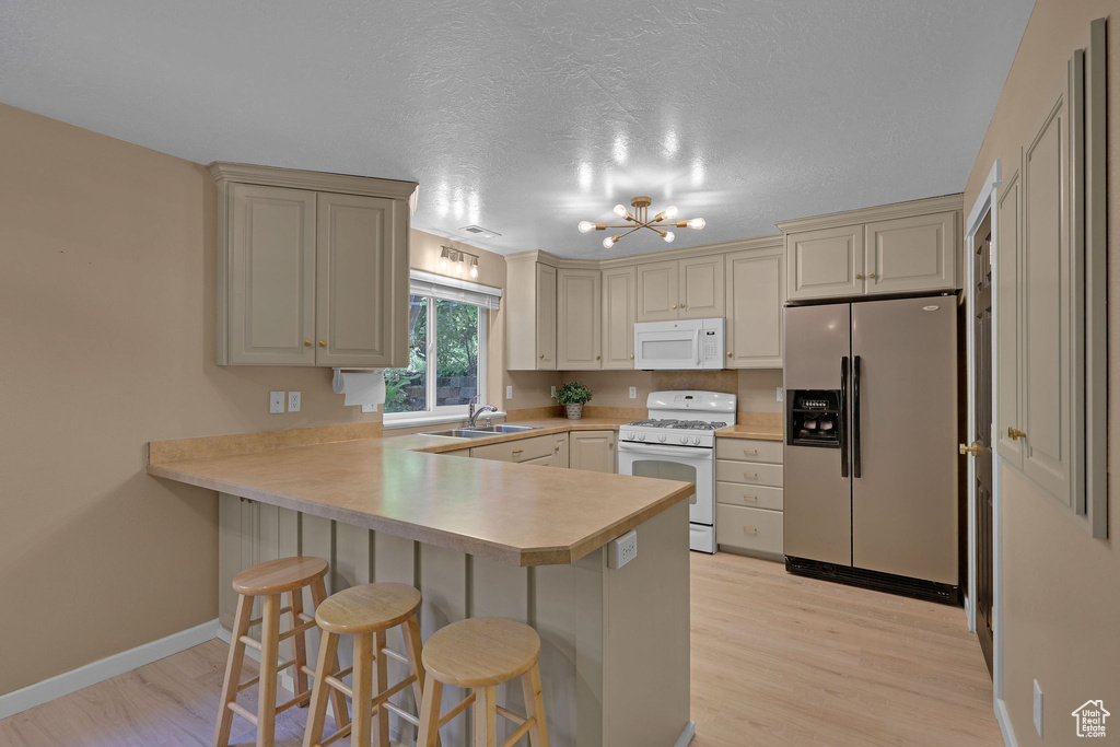 Kitchen featuring white appliances, light wood finished floors, a peninsula, a chandelier, and a breakfast bar
