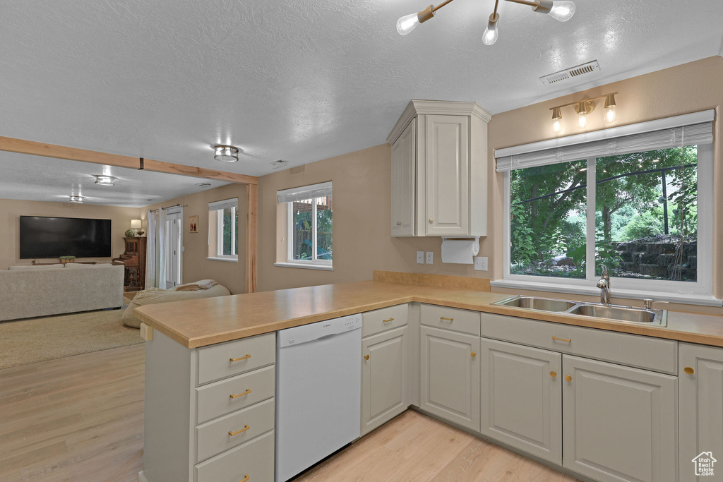 Kitchen featuring white dishwasher, a peninsula, light wood finished floors, light countertops, and a textured ceiling