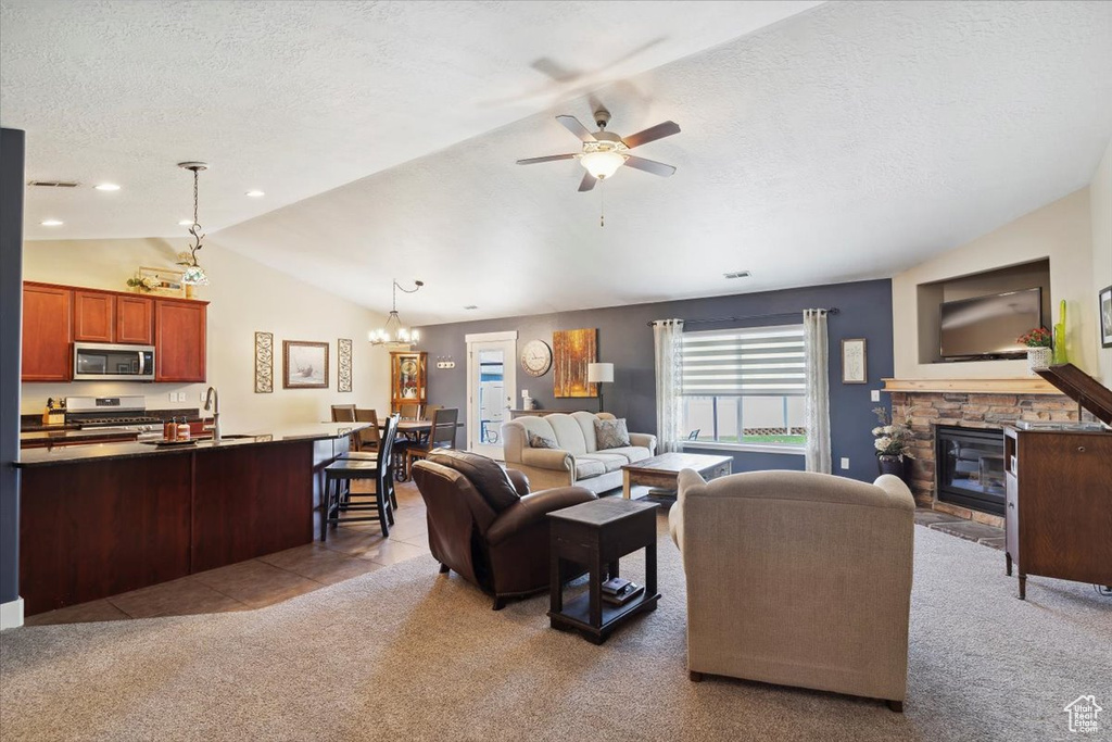 Tiled living area featuring lofted ceiling, a stone fireplace, carpet floors, a ceiling fan, and a chandelier