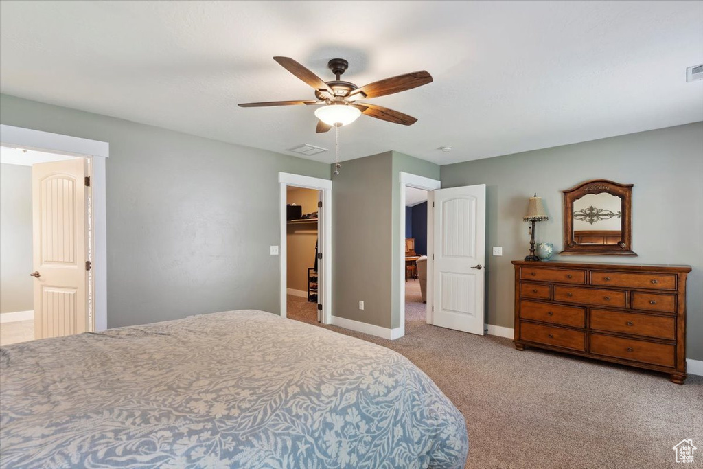 Bedroom with light colored carpet, a walk in closet, and ceiling fan